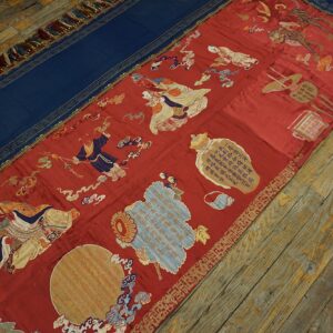 Ornate red and blue textile runner featuring embroidered figures and patterns rests on wide wooden plank floors.