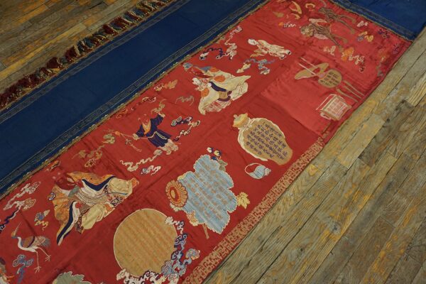 Ornate red and blue textile runner featuring embroidered figures and patterns rests on wide wooden plank floors.