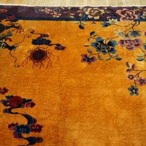Close-up showing a gold rug with a dark dragon motif and a vibrant purple floral border on wood flooring.