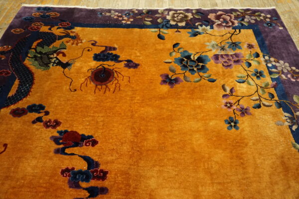 Close-up showing a gold rug with a dark dragon motif and a vibrant purple floral border on wood flooring.