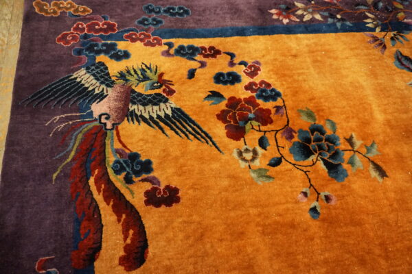 Golden orange rug with deep purple border features a stylized bird and elaborate multicolored florals.