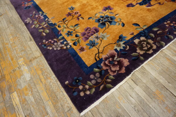 Golden-yellow floral rug with blue and purple accents features a deep purple border on worn wood flooring.