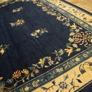 Navy blue rug with scattered yellow floral sprigs and a cream border featuring teal designs on wood flooring.