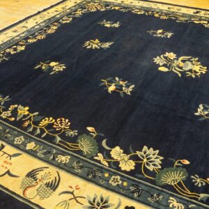 Navy floral rug with a wide gold border featuring stylized birds, displayed on light hardwood floor.