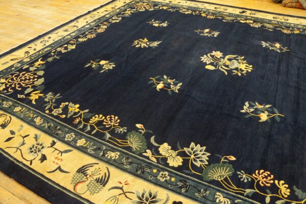 Navy floral rug with a wide gold border featuring stylized birds, displayed on light hardwood floor.