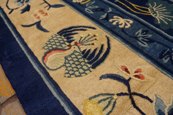 Thick-pile rug detail showing a beige field, deep blue border, and stylized bird and floral pattern.