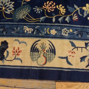 Navy blue rug with detailed floral and stylized bird border resting on rustic wood flooring.