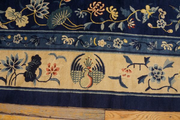 Navy blue rug with detailed floral and stylized bird border resting on rustic wood flooring.