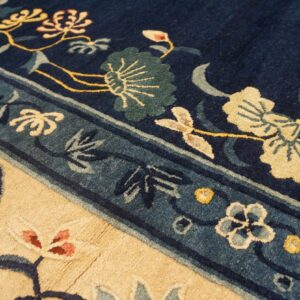 Detail shot of a rug with navy blue, beige, and teal borders framing stylized yellow and green floral patterns.