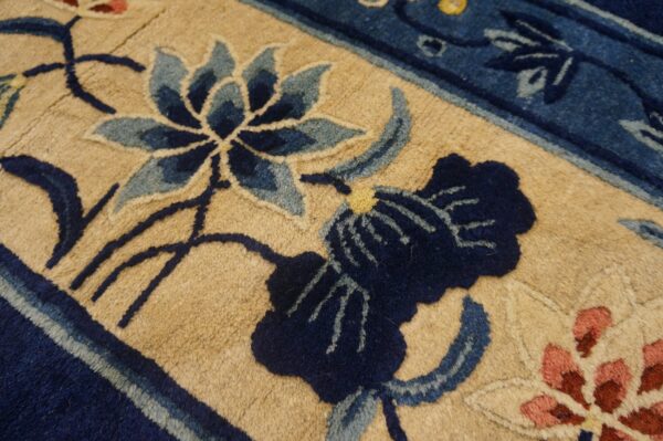 A close-up of a textured rug displays a tan background with dark and light blue botanical motifs.