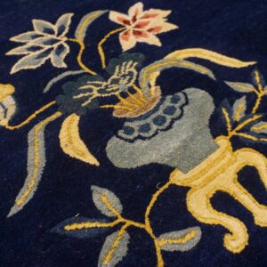 Close-up of a rug featuring a dark navy background and a colorful floral vase motif in yellow, light blue, and pink.