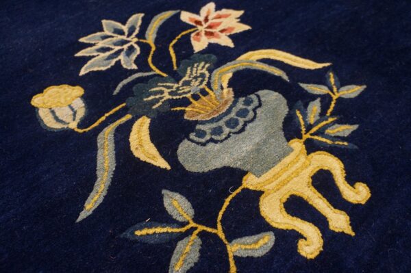 Close-up of a rug featuring a dark navy background and a colorful floral vase motif in yellow, light blue, and pink.