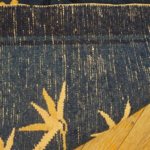Close-up of a rolled navy blue rug featuring cream floral accents on natural wood plank flooring.