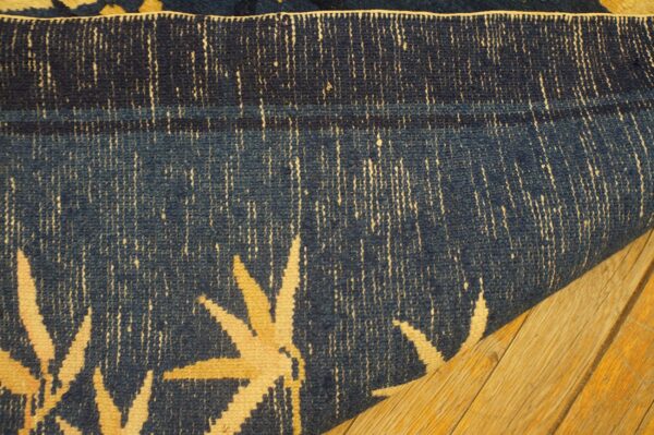 Close-up of a rolled navy blue rug featuring cream floral accents on natural wood plank flooring.