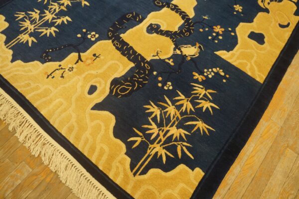 Close-up of a blue and gold rug featuring a snake, bird, bamboo, and carved fringe detail on wood floor.