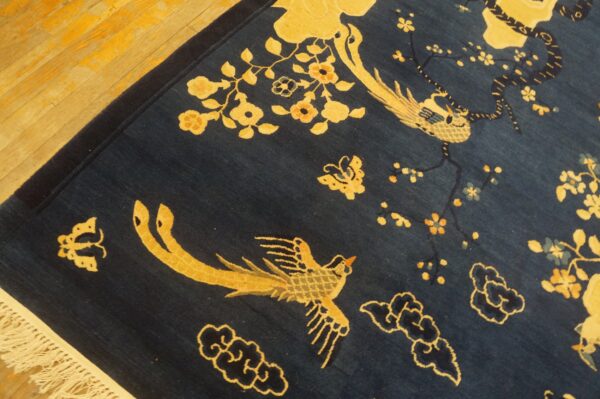 A dark blue rug with gold birds and flowers rests on light hardwood flooring, showing fringe.