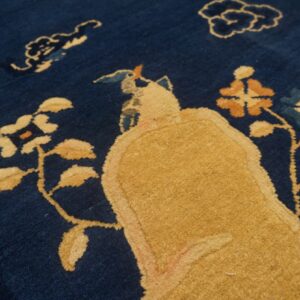 A deep blue rug features a golden yellow stylized figure and rust and light blue floral motifs.