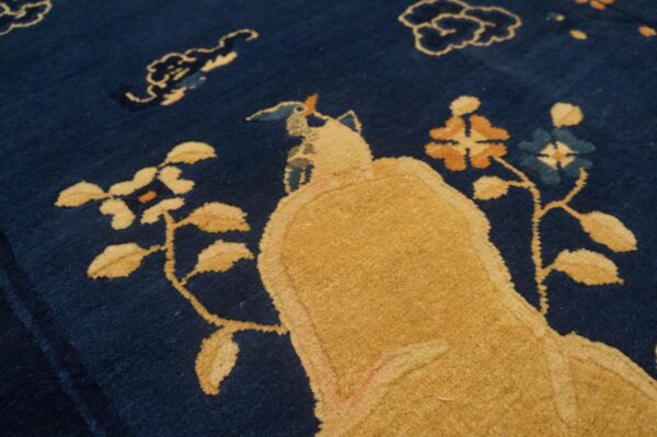 A deep blue rug features a golden yellow stylized figure and rust and light blue floral motifs.