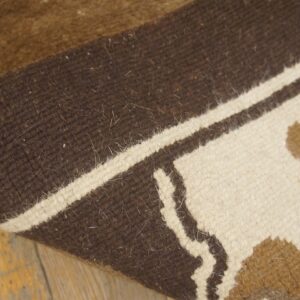 Curled brown, white, and tan patterned rug rests on distressed wooden floorboards.