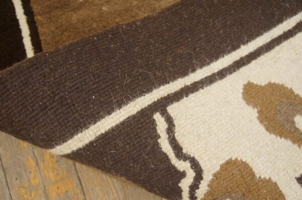 Curled brown, white, and tan patterned rug rests on distressed wooden floorboards.