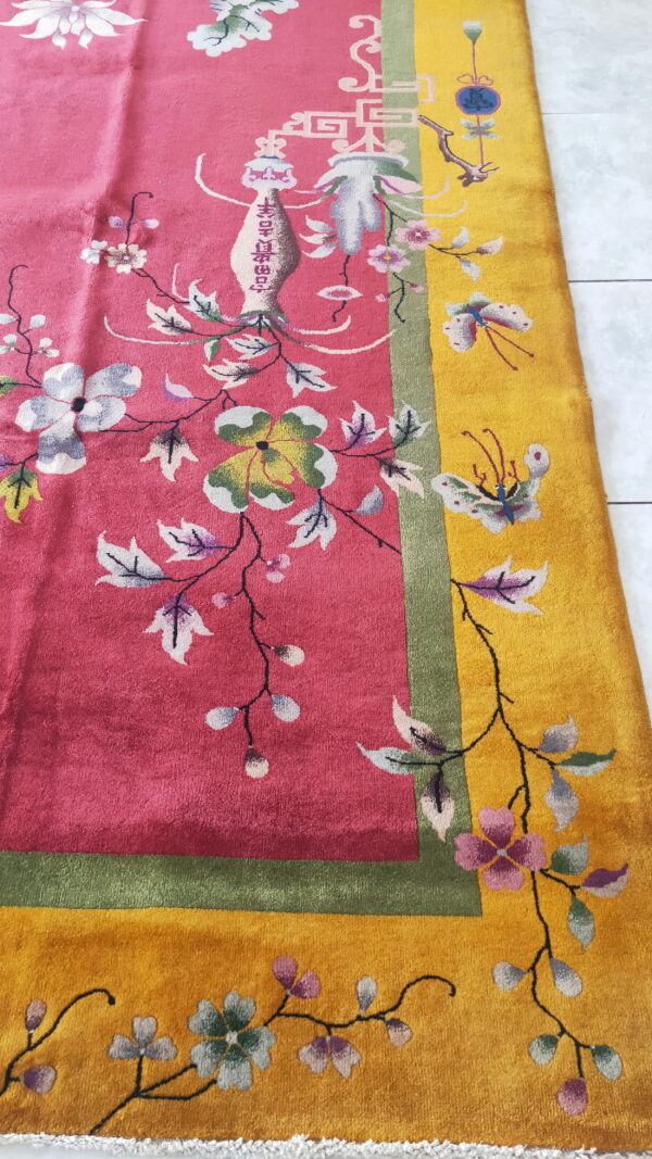 High-pile pink rug with detailed florals and a golden yellow border on a white tiled floor.