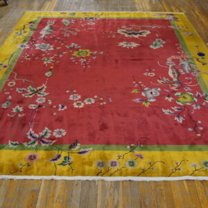 Vibrant red rug with green and yellow border, featuring pastel floral vines on a wood floor.