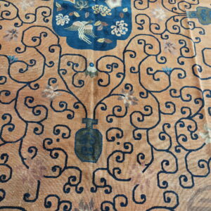 Faded orange rug with dark blue vine scrolls surrounding a blue medallion featuring a bird and flowers.