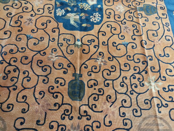 Faded orange rug with dark blue vine scrolls surrounding a blue medallion featuring a bird and flowers.