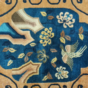 Close-up of a rug featuring an intricate blue medallion with floral and bird motifs on a gold field.