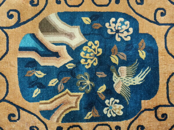 Close-up of a rug featuring an intricate blue medallion with floral and bird motifs on a gold field.