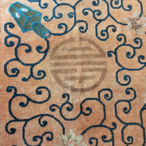 Close-up of a rug section featuring a peach field, teal border, dark scrolling patterns, and a worn central motif.