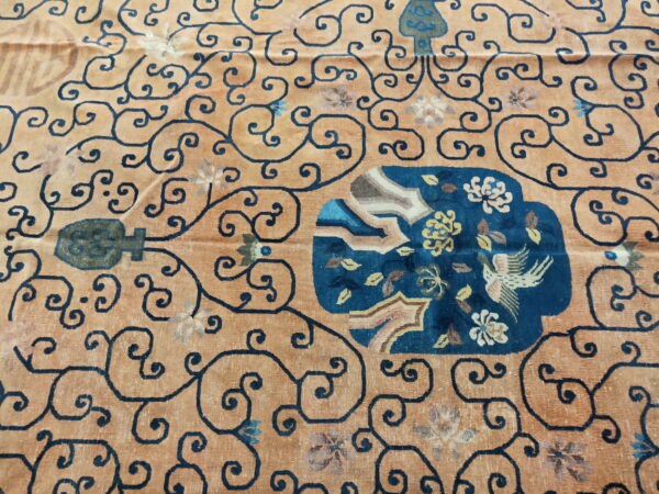 Apricot rug with dark blue scrolling vines surrounding a central blue panel depicting flowers and a bird.