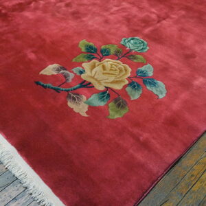 Plush crimson rug on distressed hardwood features a large floral spray with yellow and blue roses.