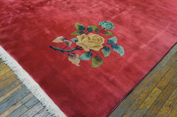 Plush crimson rug on distressed hardwood features a large floral spray with yellow and blue roses.
