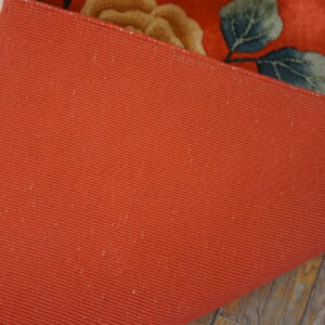 Close-up showing the terracotta ribbed backing of a floral rug lying on gray wood floors.