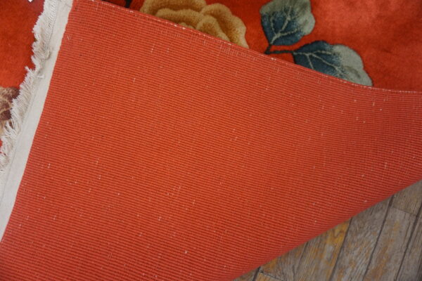 Close-up showing the terracotta ribbed backing of a floral rug lying on gray wood floors.