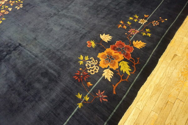 Velvety dark blue rug featuring large autumn-toned floral vines and a striped border on light wood flooring.
