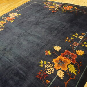 Deep blue rug with bright floral corner motifs in rust, gold, and green on a polished wood floor.