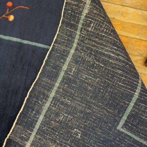 A navy low-pile rug showing a small orange design is folded back on rustic wooden flooring.