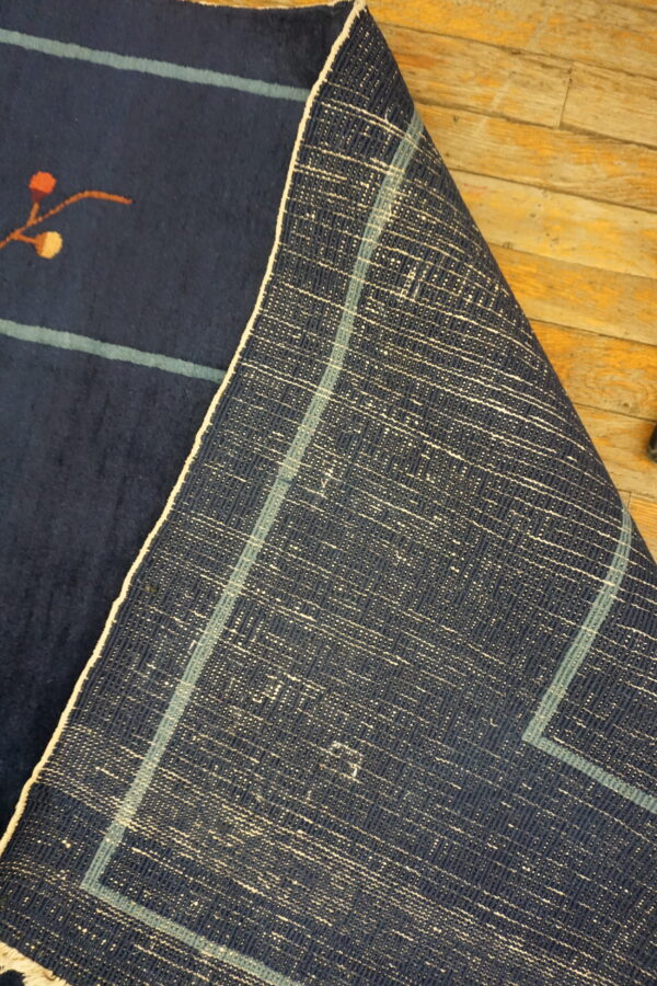 A navy low-pile rug showing a small orange design is folded back on rustic wooden flooring.