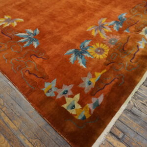 Plush rust-colored rug with light blue and yellow botanical designs rests on worn wooden plank flooring.