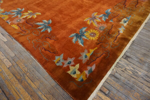 Plush rust-colored rug with light blue and yellow botanical designs rests on worn wooden plank flooring.