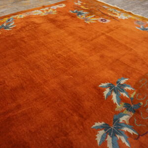 Velvety orange rug features a decorative border of blue leaves and floral motifs on wood planks.