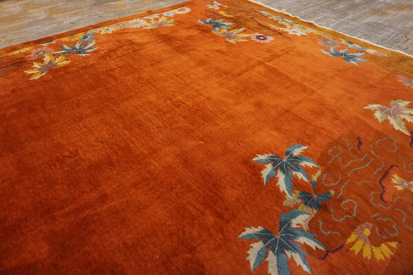Velvety orange rug features a decorative border of blue leaves and floral motifs on wood planks.