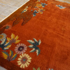 Rust-colored plush rug with a colorful floral and leaf border resting on distressed wood flooring.
