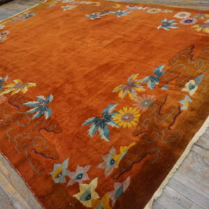 A high-sheen rust rug with a bright floral border is displayed on worn gray wooden planks.