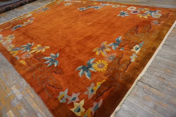 A high-sheen rust rug with a bright floral border is displayed on worn gray wooden planks.