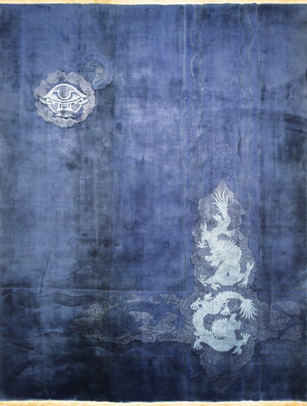 Plush blue rug displaying light gray dragon and cloud motifs with a monogram, laid on wood planks.