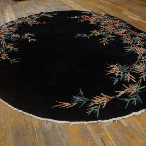 Round black rug with a plush pile and botanical borders in teal, tan, and pink on wood planks.