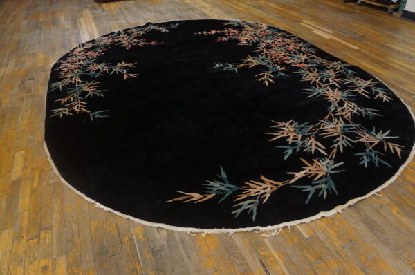 Round black rug with a plush pile and botanical borders in teal, tan, and pink on wood planks.
